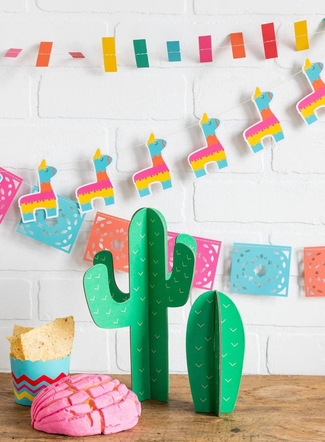 Decorative cactus with colorful pinata decorations on a white wall.
