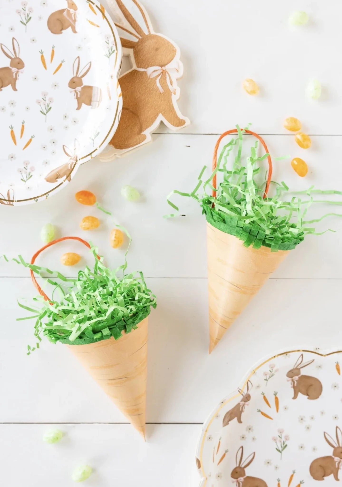 Carrot-shaped cones with green grass on a white surface with bunny-themed plates.