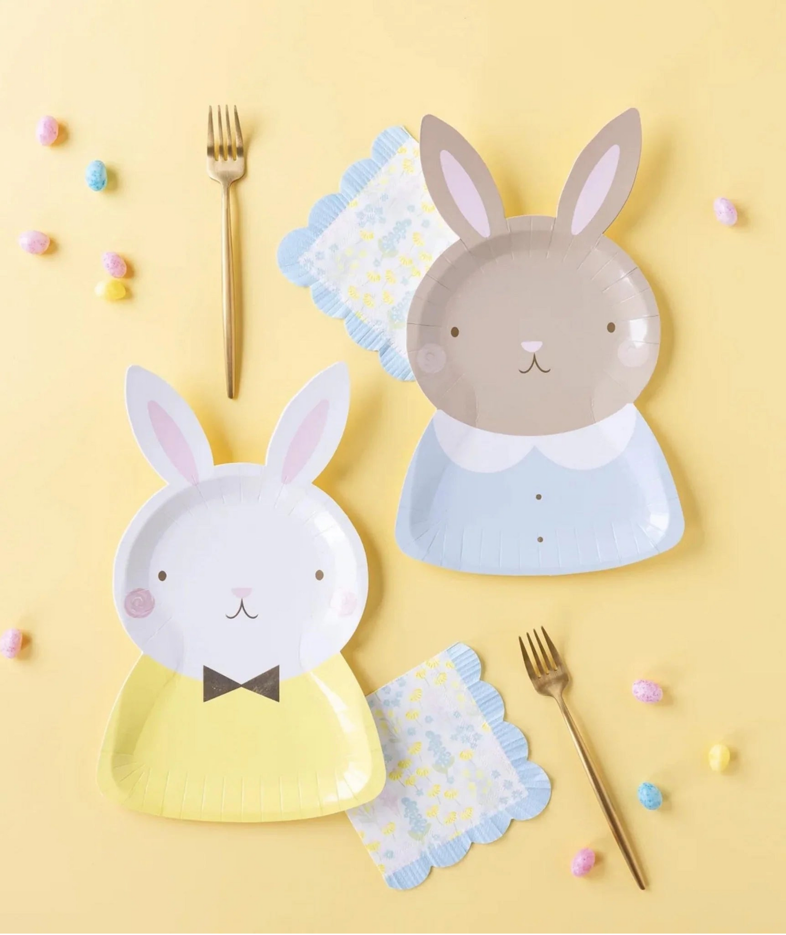Two rabbit-shaped plates on a yellow background with gold forks and colorful candies.